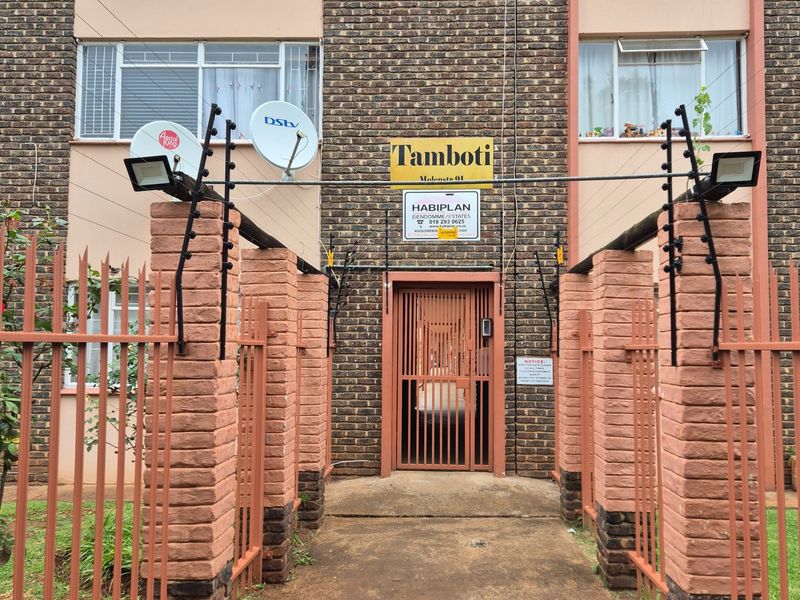 Front entrance view of the apartment complex featuring a brick facade, secure gated access, and perimeter electric fencing.