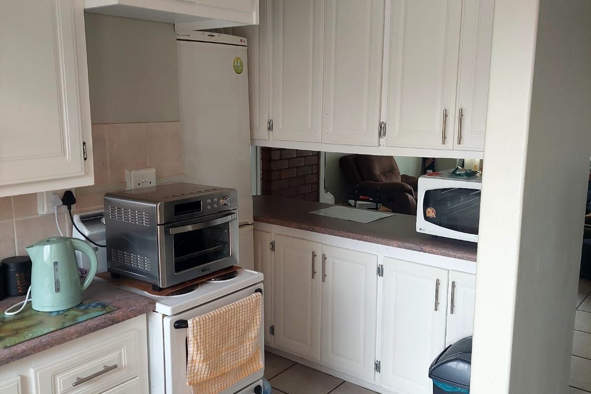 A functional kitchen featuring white built-in cabinetry, tiled flooring, and a tiled backsplash, offering a practical layout with ample storage space.