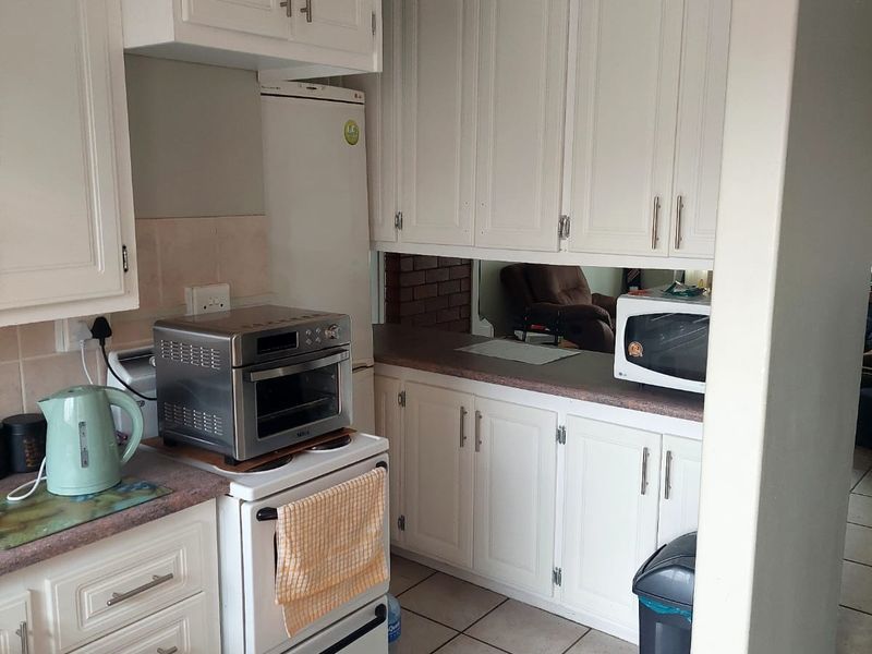 A functional kitchen featuring white built-in cabinetry, tiled flooring, and a tiled backsplash, offering a practical layout with ample storage space.