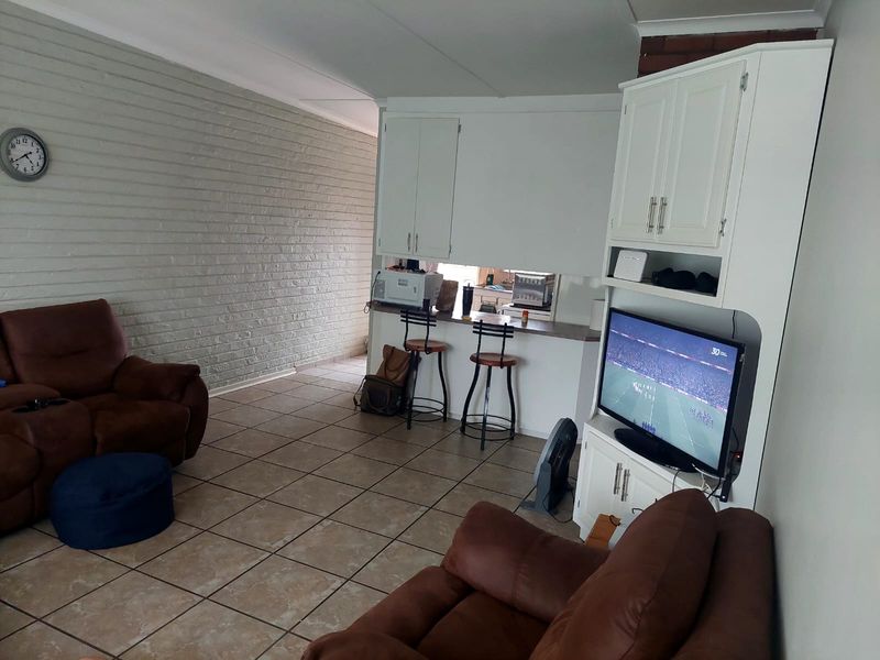 Open-plan living area featuring a breakfast bar, built-in cabinetry, tiled flooring, and a textured brick feature wall.