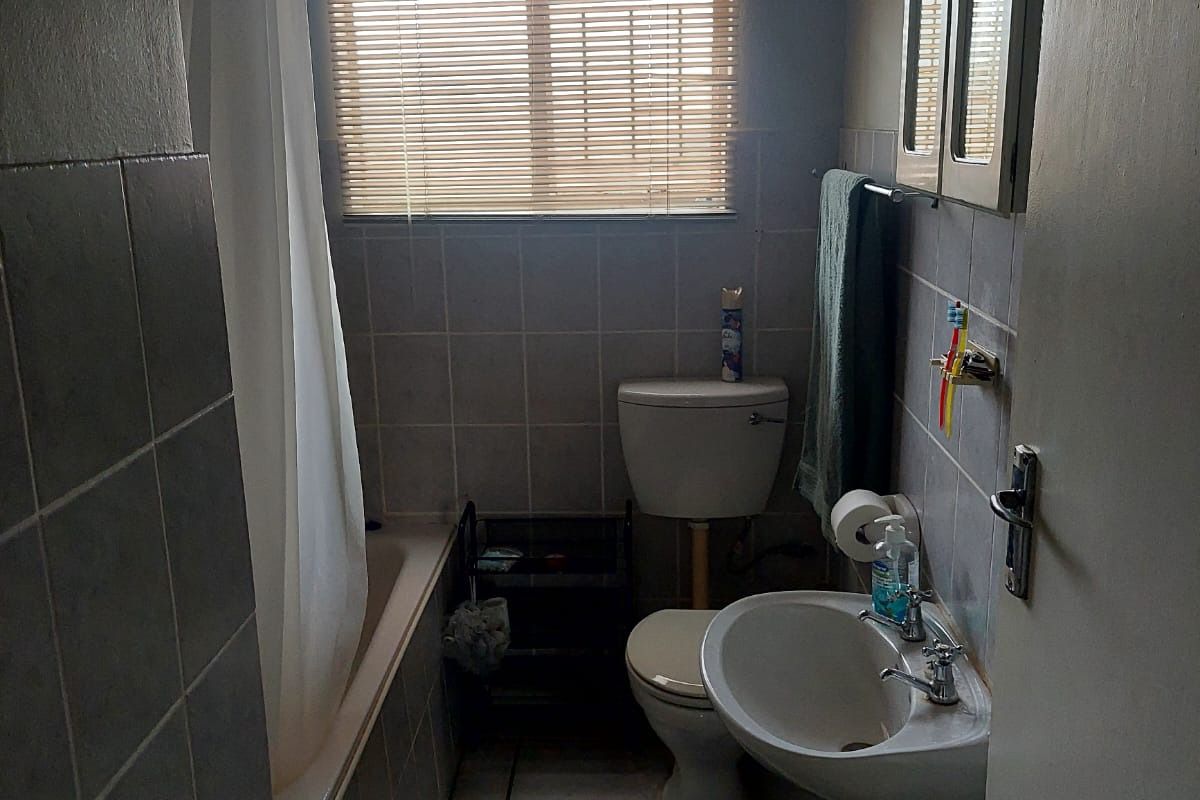 A compact bathroom featuring a bathtub, pedestal basin, and toilet with tiled finishes, requiring some cosmetic updates to improve its overall condition.