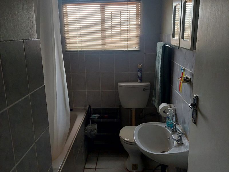 A compact bathroom featuring a bathtub, pedestal basin, and toilet with tiled finishes, requiring some cosmetic updates to improve its overall condition.