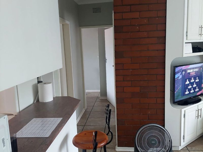 Open plan living area featuring an exposed brick wall, built-in cabinetry, and tiled flooring, providing a functional layout with direct access to the hallway.