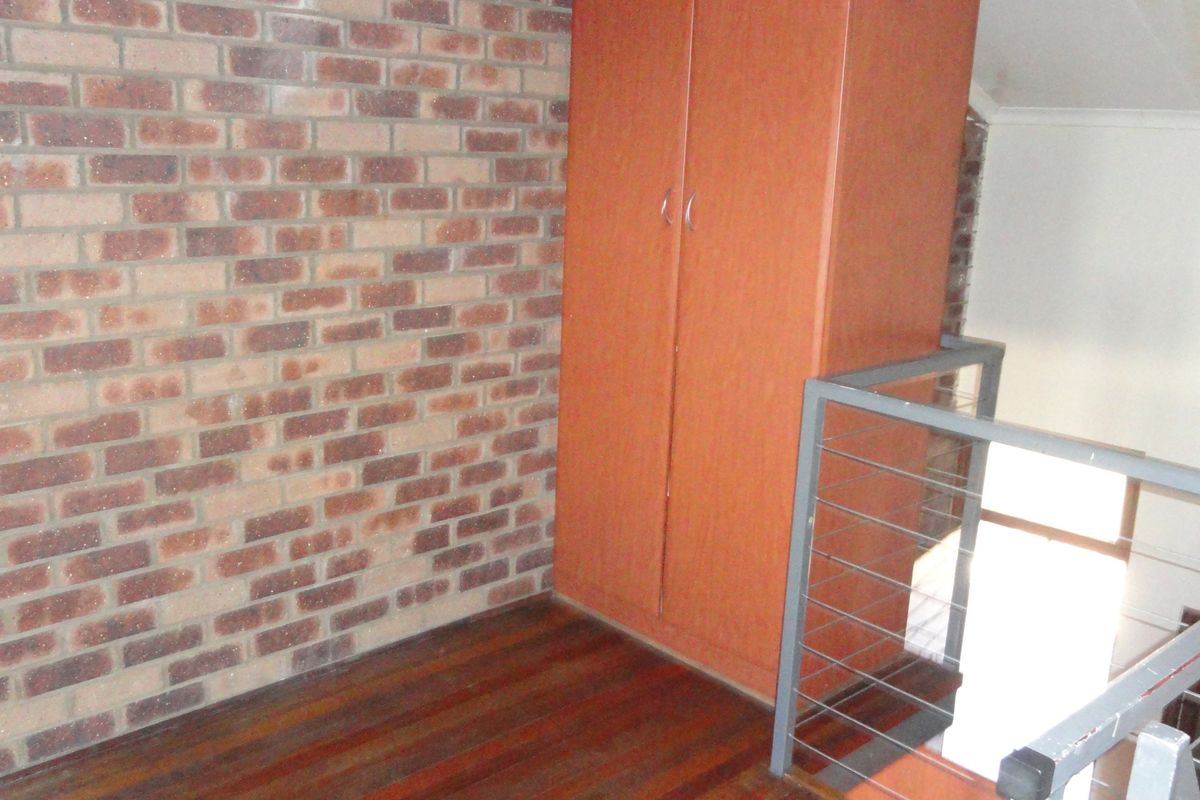 A bedroom area featuring exposed brickwork, timber flooring, and a built-in wardrobe, adjacent to a metal staircase balustrade.