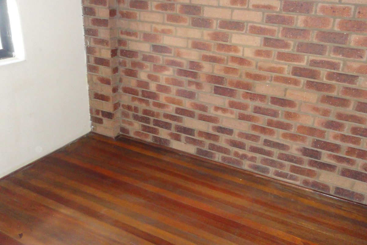 An empty bedroom featuring a characterful exposed brick feature wall and polished timber flooring.