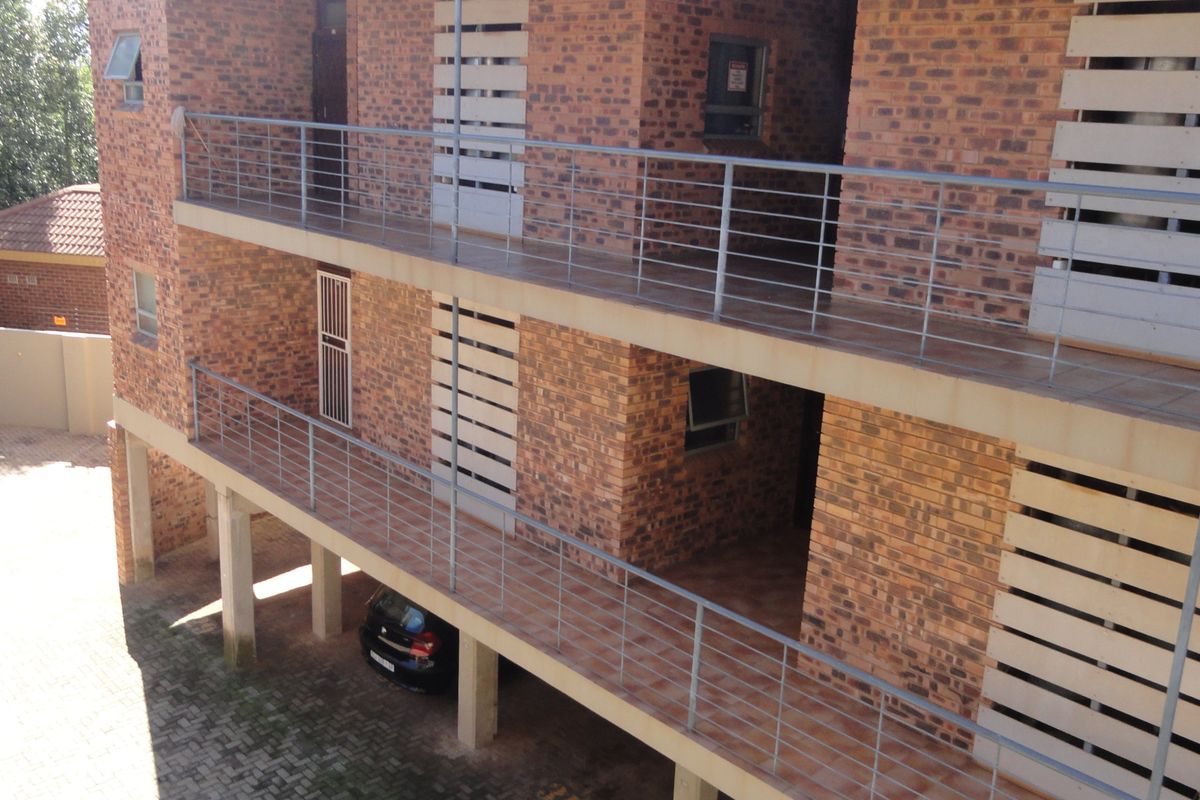 Exterior view of a multi-story apartment building featuring exposed brickwork, metal balustrades, and covered balcony walkways with ground-level parking.