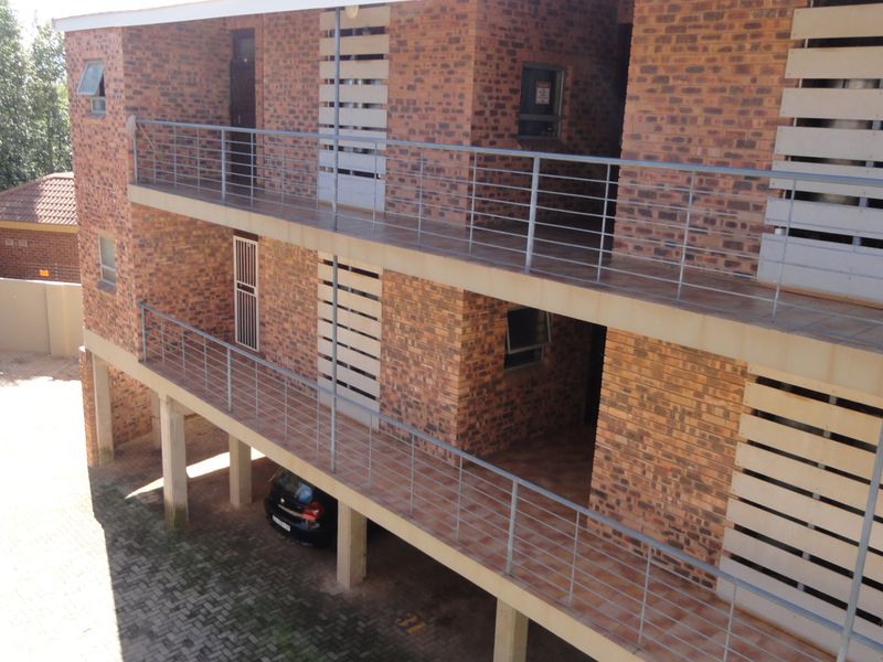 Exterior view of a multi-story apartment building featuring exposed brickwork, metal balustrades, and covered balcony walkways with ground-level parking.