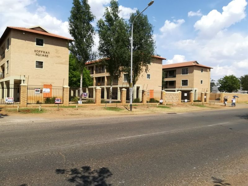 Street view of Hoffman Square apartment complex featuring multi-story brick buildings with tiled roofs and perimeter security fencing.