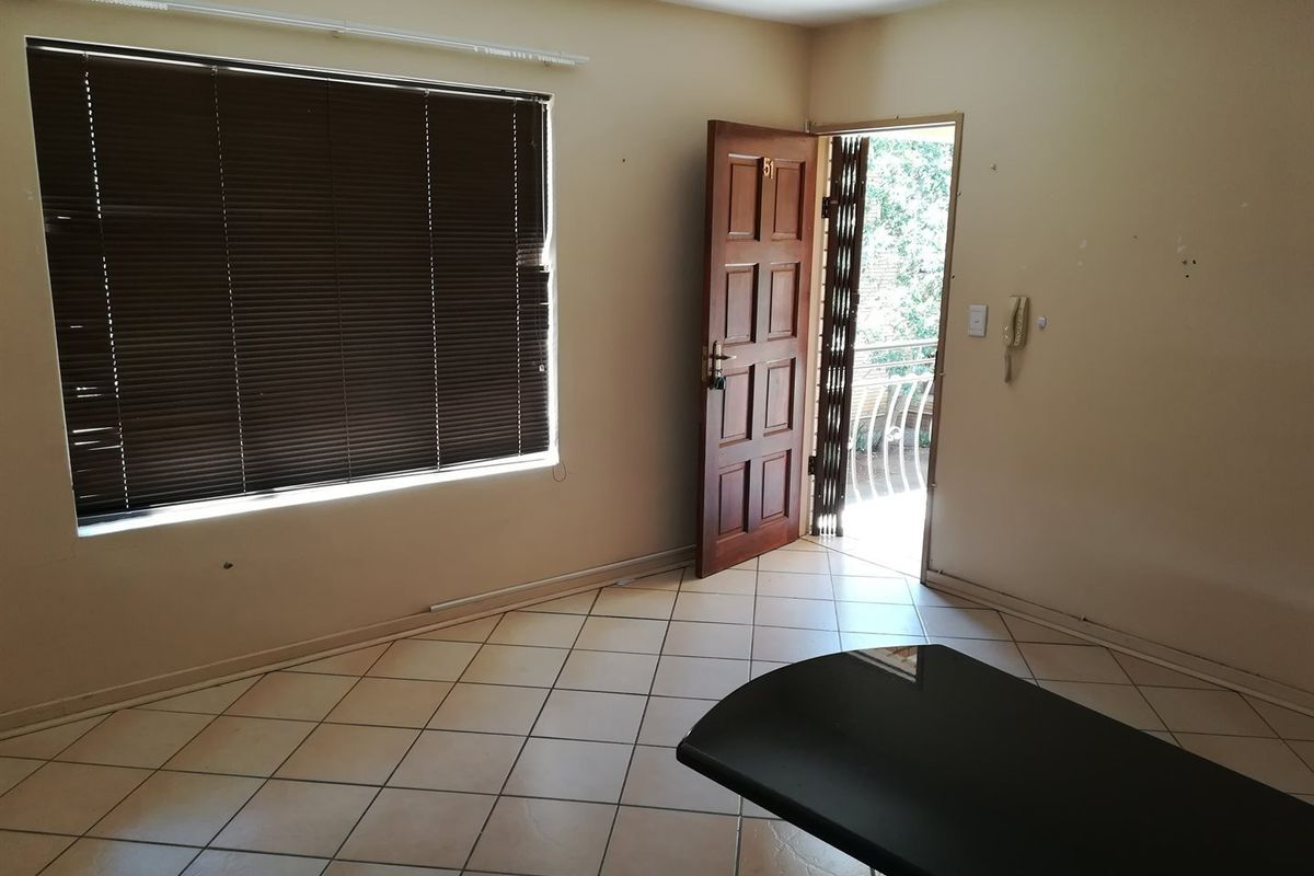An empty living area featuring tiled flooring, venetian blinds, and direct access to an outdoor balcony through a security gate.