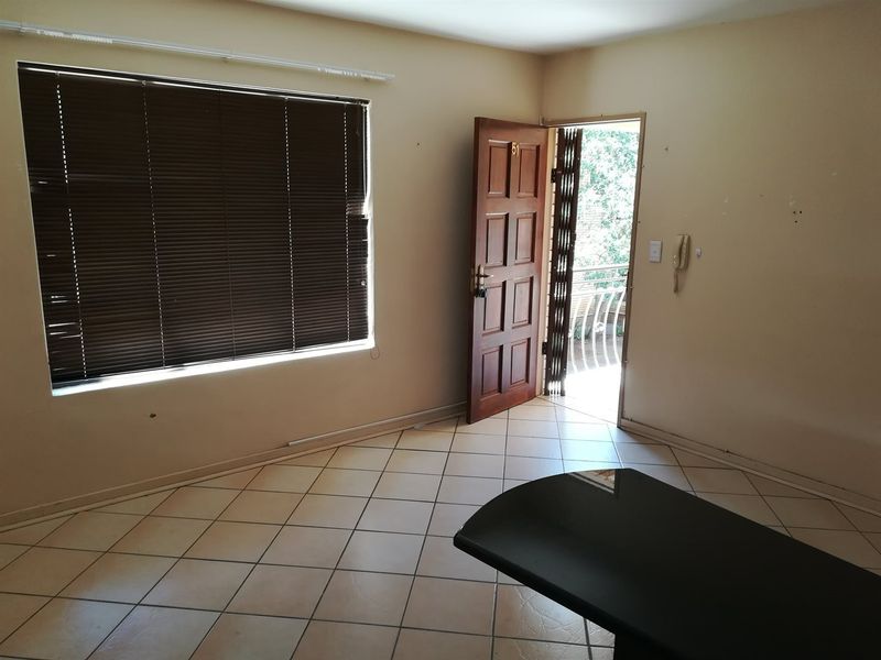 An empty living area featuring tiled flooring, venetian blinds, and direct access to an outdoor balcony through a security gate.