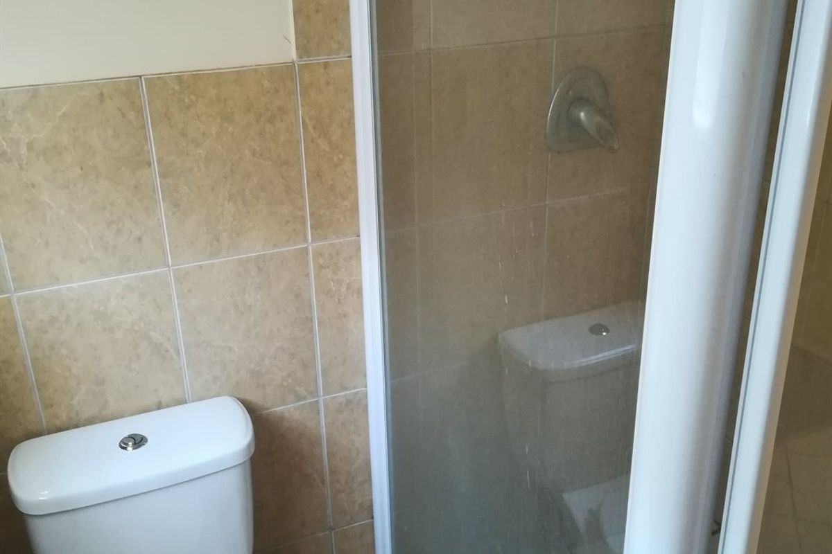 A functional bathroom featuring a shower enclosure with glass door and a standard toilet, finished with neutral ceramic wall tiling.