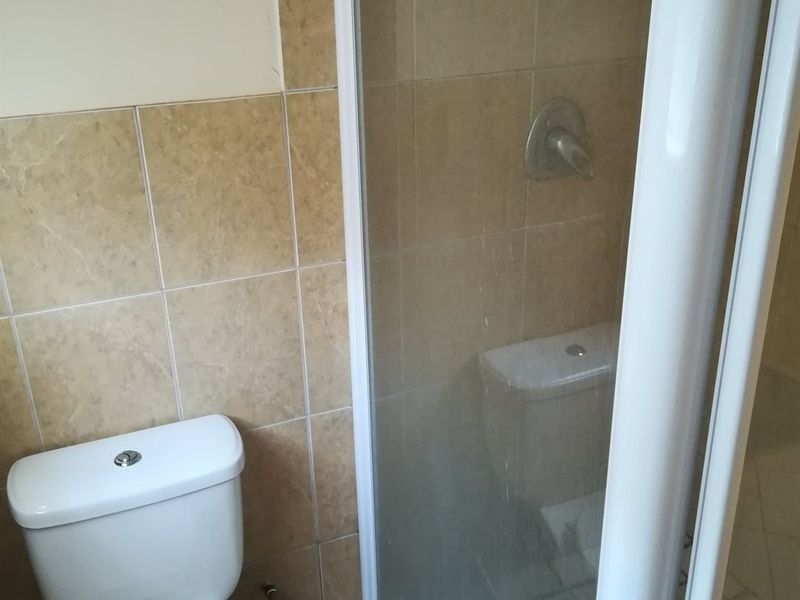 A functional bathroom featuring a shower enclosure with glass door and a standard toilet, finished with neutral ceramic wall tiling.