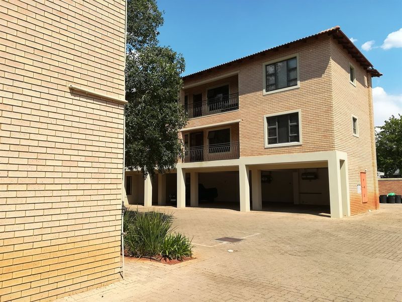 Exterior view of a multi-story apartment building featuring face brick construction, covered ground-level parking, and private balconies.