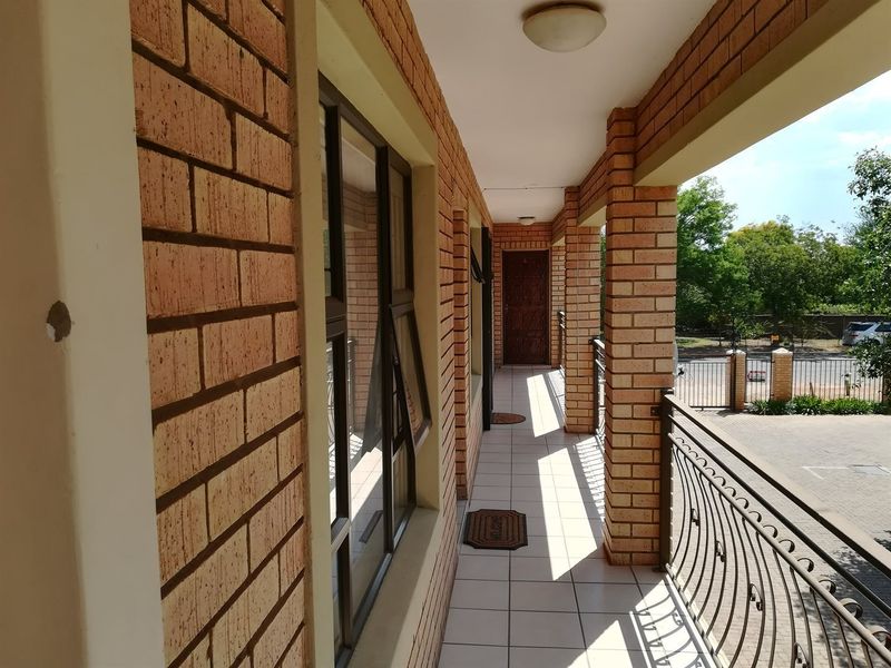 A covered balcony featuring face brick walls, tiled flooring, and a wrought iron balustrade overlooking the property entrance.