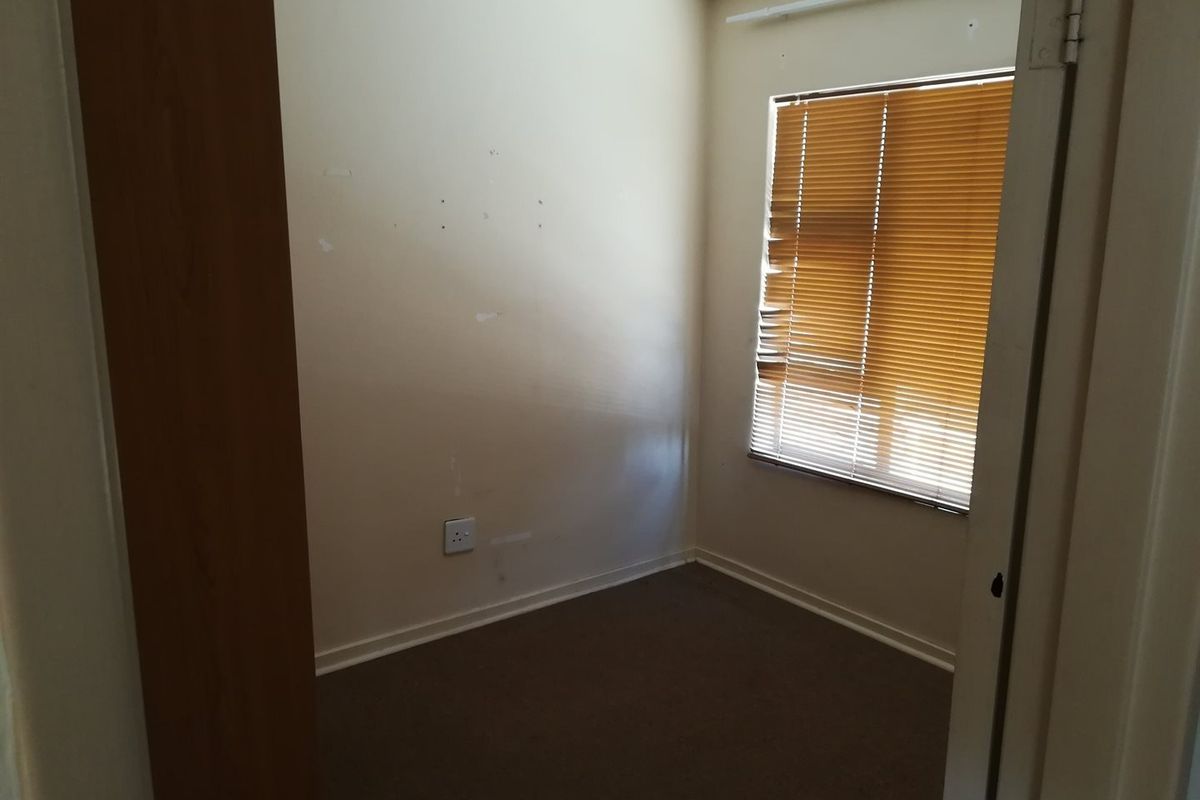 An empty bedroom featuring carpet flooring, a window with damaged venetian blinds, and wall scuffs requiring maintenance.