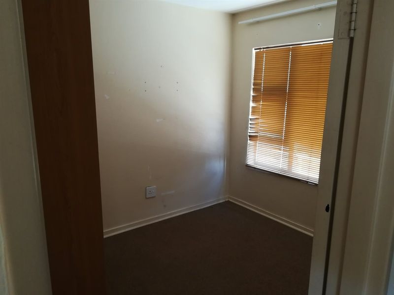 An empty bedroom featuring carpet flooring, a window with damaged venetian blinds, and wall scuffs requiring maintenance.