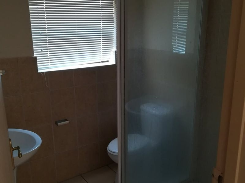 A functional bathroom featuring a shower enclosure, toilet, and tiled finishes, currently presented in a basic, dated condition.