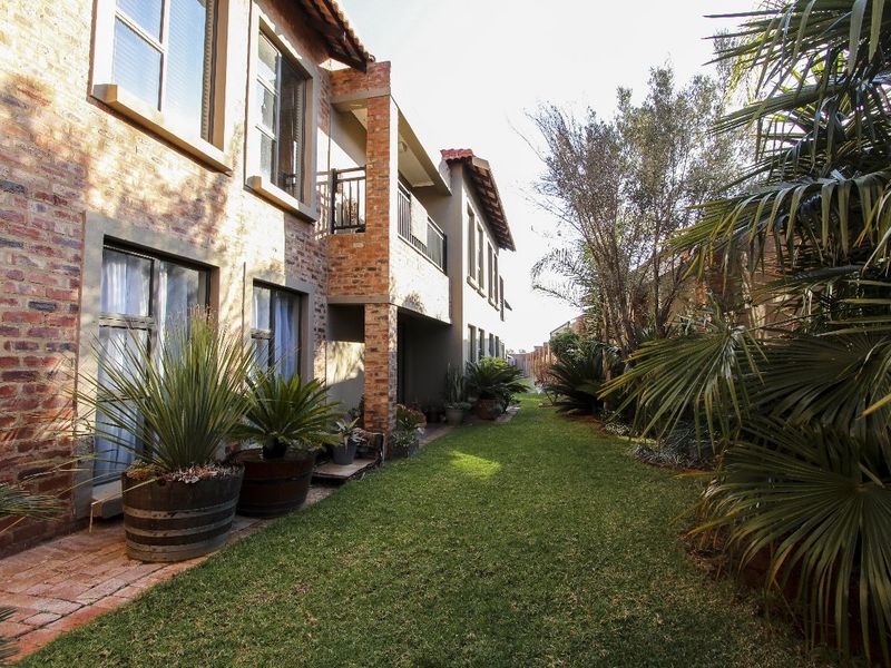 A well-maintained rear exterior view of the apartment building featuring a face brick facade, a private balcony, and a lush landscaped garden.