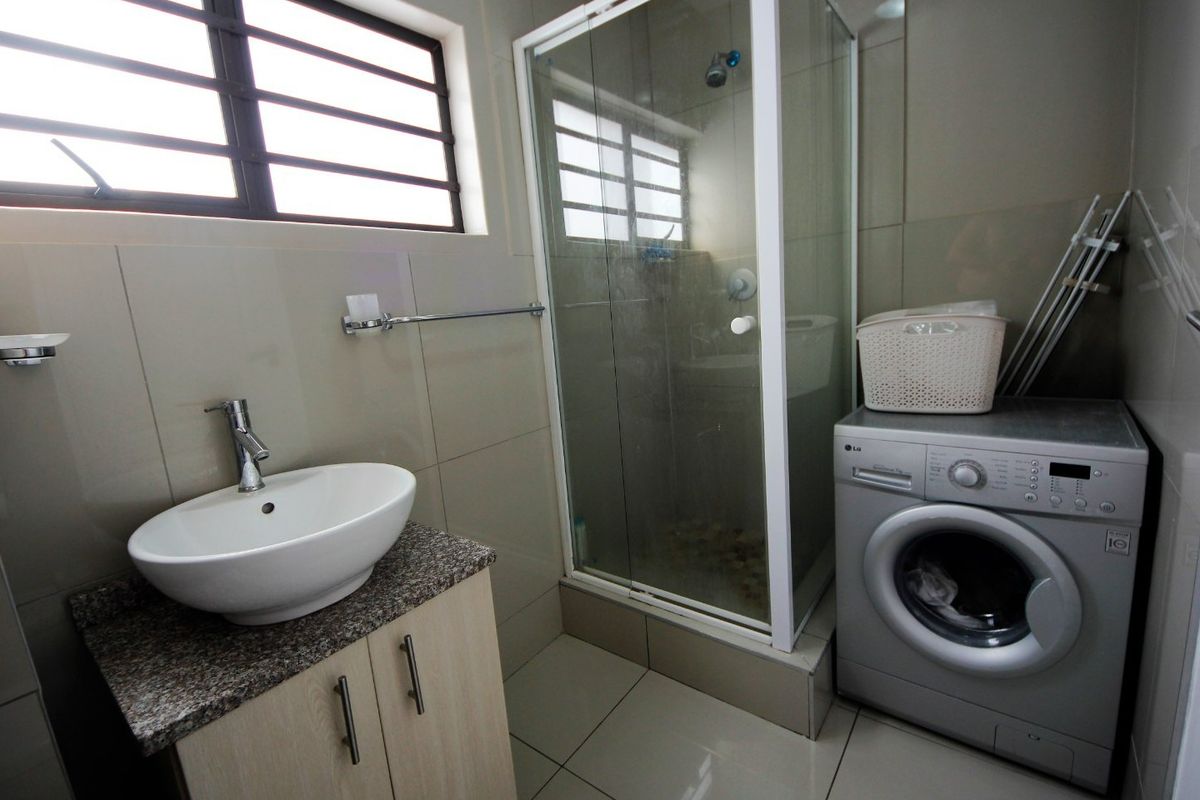 A modern bathroom featuring a vessel sink on a granite vanity, a glass shower enclosure, and neutral wall and floor tiling.
