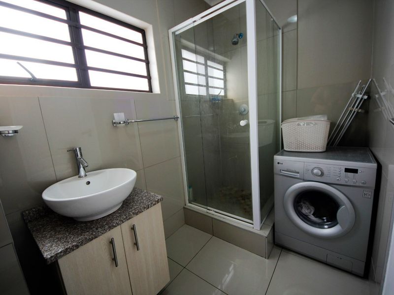 A modern bathroom featuring a vessel sink on a granite vanity, a glass shower enclosure, and neutral wall and floor tiling.