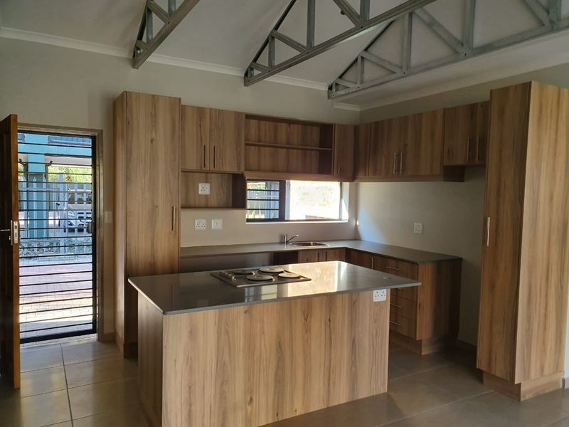 Modern kitchen featuring wood-finish cabinetry, a central island with a built-in hob, stainless steel sink, and exposed industrial-style roof trusses.