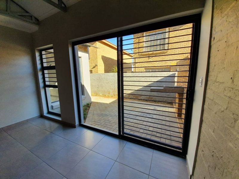Bright living area featuring tiled floors, an exposed roof truss, a brick feature wall, and sliding doors opening to a paved patio.