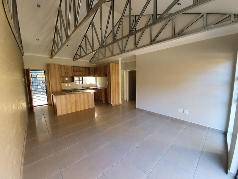 Spacious open-plan living and kitchen area featuring modern wood-finish cabinetry, tiled floors, and striking exposed steel roof trusses in a contemporary townhouse setting.