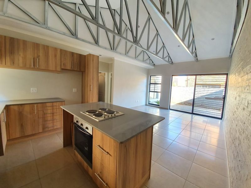 Spacious open-plan kitchen and living area featuring modern cabinetry, a central island with built-in appliances, exposed steel trusses, and large sliding doors to the exterior.