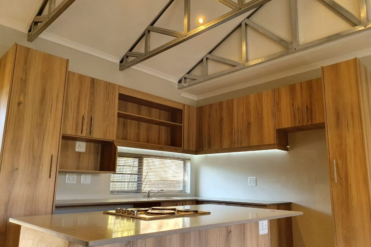 Modern kitchen featuring wood-look cabinetry, stone countertops, a built-in gas hob, and striking exposed metal roof trusses for a contemporary industrial aesthetic.