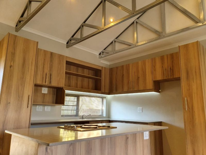 Modern kitchen featuring wood-look cabinetry, stone countertops, a built-in gas hob, and striking exposed metal roof trusses for a contemporary industrial aesthetic.