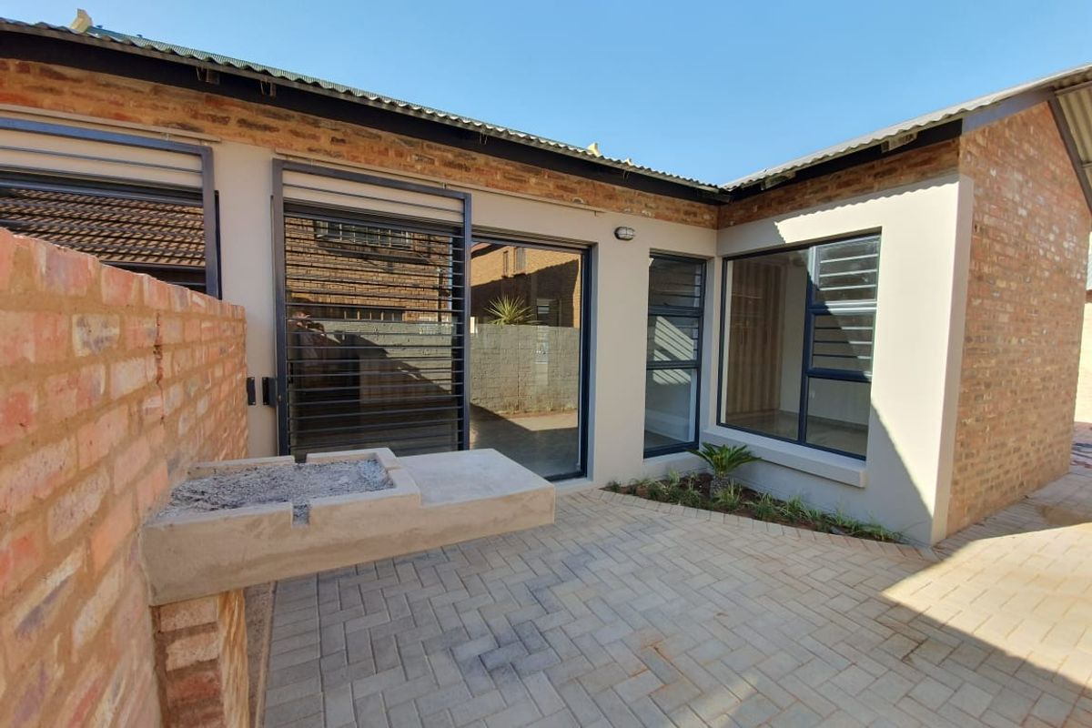 A neat rear courtyard featuring brick paving, a built-in braai, and modern aluminium-framed windows and sliding doors.