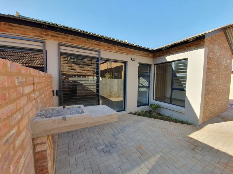A neat rear courtyard featuring brick paving, a built-in braai, and modern aluminium-framed windows and sliding doors.