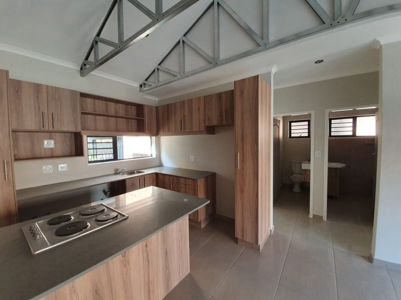 Modern kitchen featuring wood-look cabinetry, integrated hob, and exposed steel roof trusses, with an adjacent bathroom visible in the background.