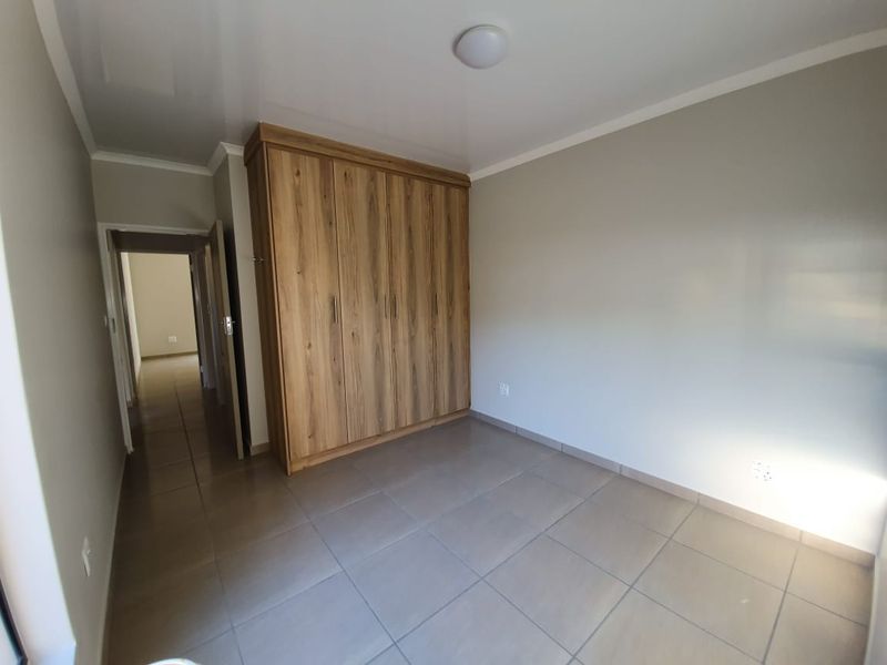 A clean, empty bedroom featuring neutral tiled flooring, built-in wooden cupboards, and a simple ceiling light fixture.