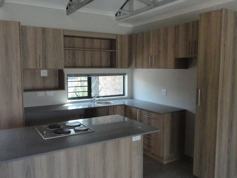 A functional kitchen featuring wood-look cabinetry, dark countertops, and a built-in electric hob, with an open-ceiling design showing exposed roof trusses.