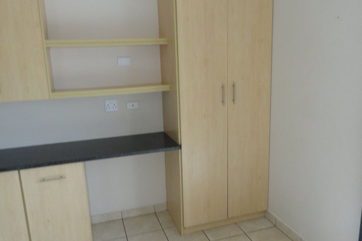 A bedroom featuring light wood built-in cupboards and a matching integrated desk with a dark countertop, set against neutral walls and tiled flooring.