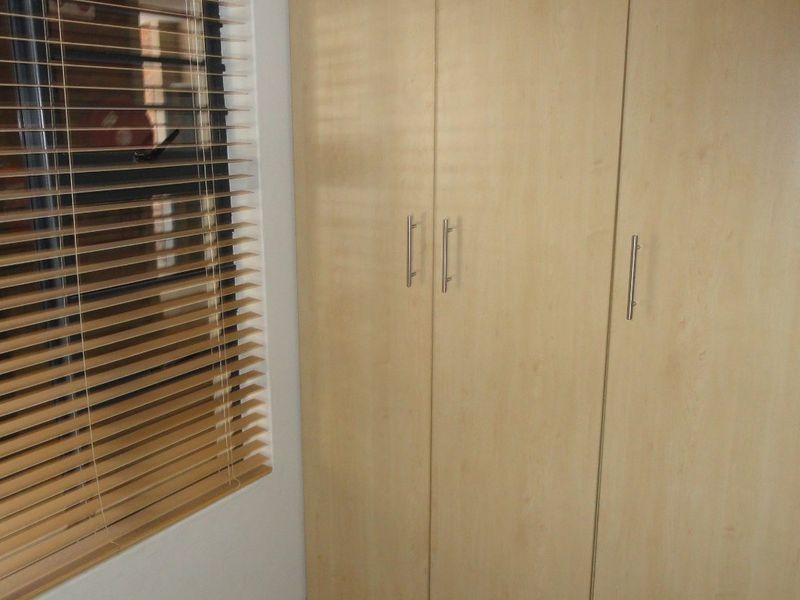A bedroom featuring light wood-finish built-in wardrobes and venetian blinds on the window.