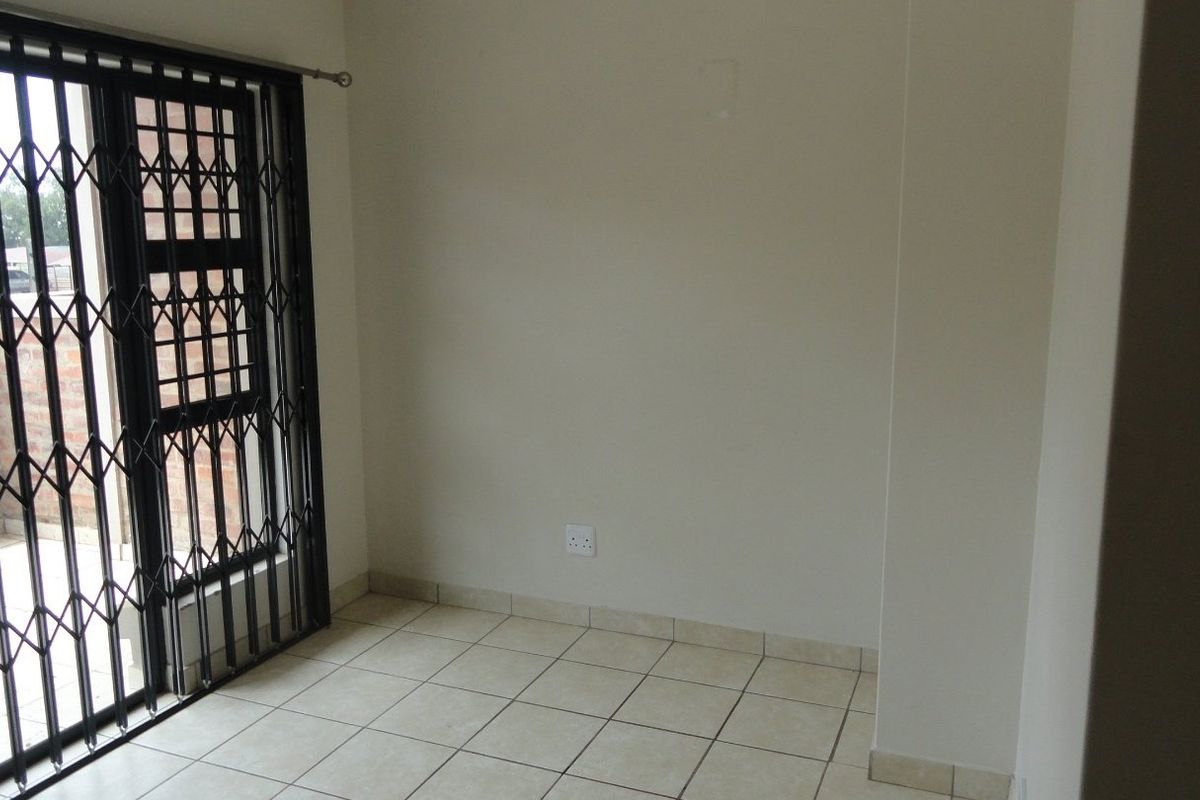 An empty living area featuring neutral tiled flooring and a secure sliding door leading to an outdoor space.