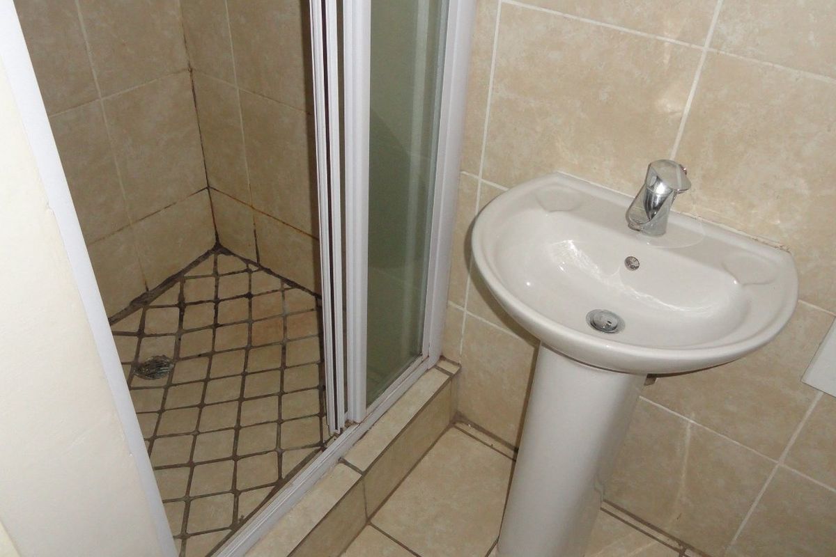 A compact bathroom featuring a pedestal basin with a chrome mixer tap and a shower enclosure with tiled finishes.