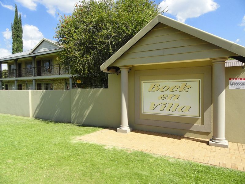 Front entrance view of the Boek en Villa apartment complex featuring a paved walkway, boundary wall, and established landscaping.