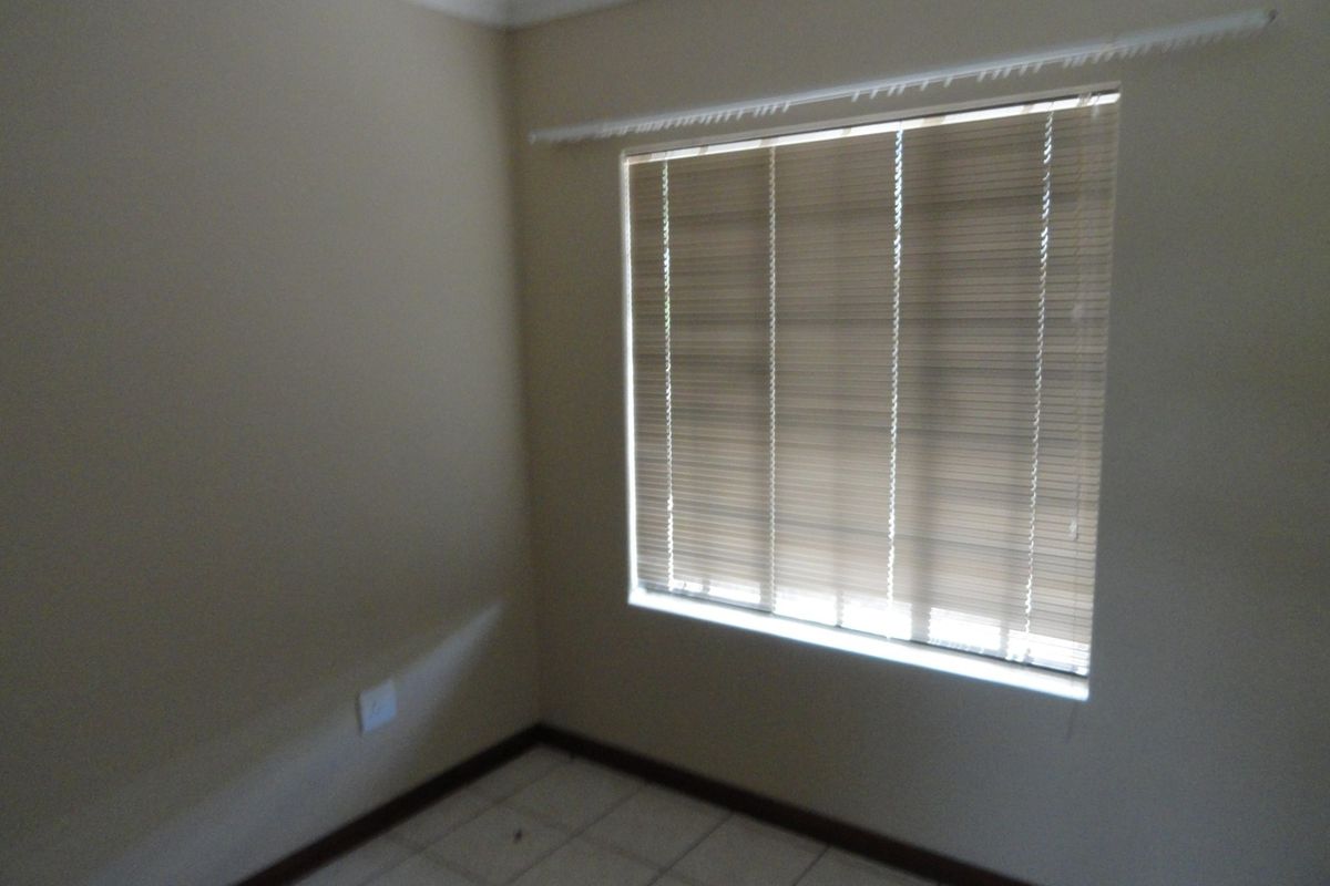 An empty bedroom featuring tiled flooring, neutral wall paint, and fitted venetian blinds, providing a blank canvas for personalization.