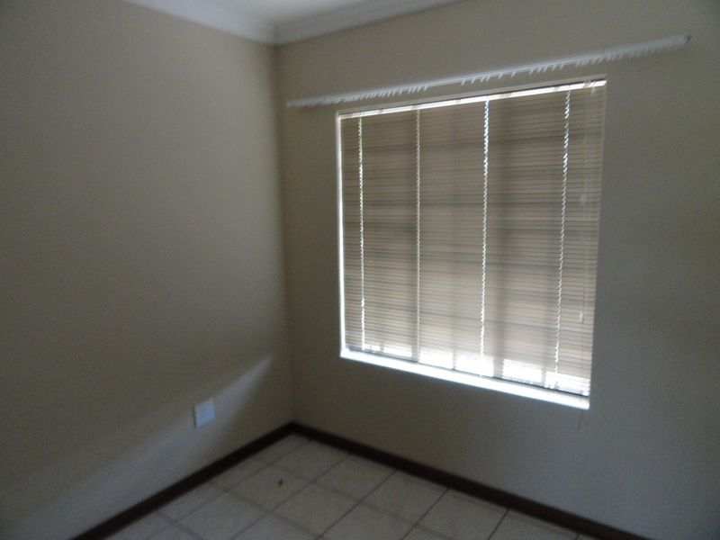 An empty bedroom featuring tiled flooring, neutral wall paint, and fitted venetian blinds, providing a blank canvas for personalization.