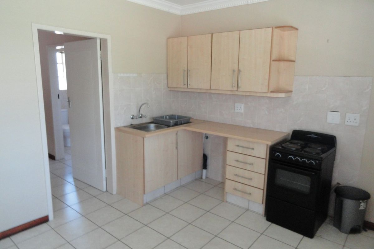 A functional kitchen featuring light wood-finish cabinetry, tiled backsplash, ceramic floor tiles, and a freestanding stove, with an adjacent doorway leading to a bathroom.