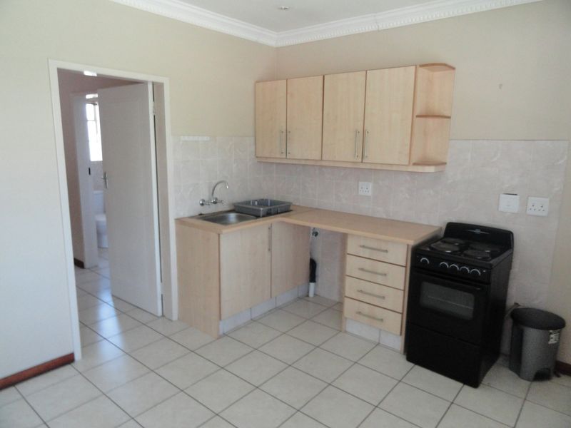 A functional kitchen featuring light wood-finish cabinetry, tiled backsplash, ceramic floor tiles, and a freestanding stove, with an adjacent doorway leading to a bathroom.