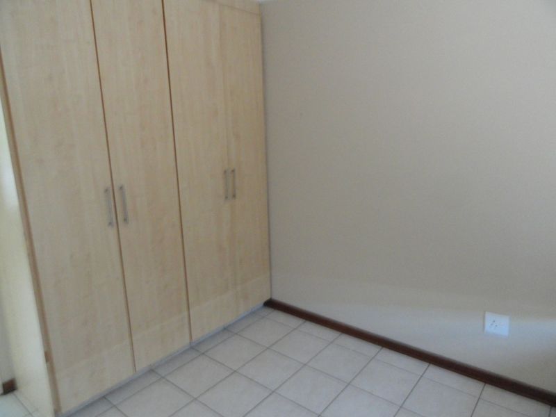 A clean, empty bedroom featuring light wood-finish built-in wardrobes and neutral tiled flooring, providing a versatile space ready for personalization.