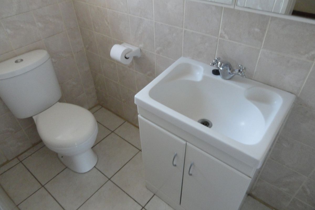 A functional bathroom featuring a white vanity basin, toilet, and neutral wall and floor tiling.