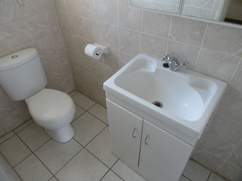 A functional bathroom featuring a white vanity basin, toilet, and neutral wall and floor tiling.