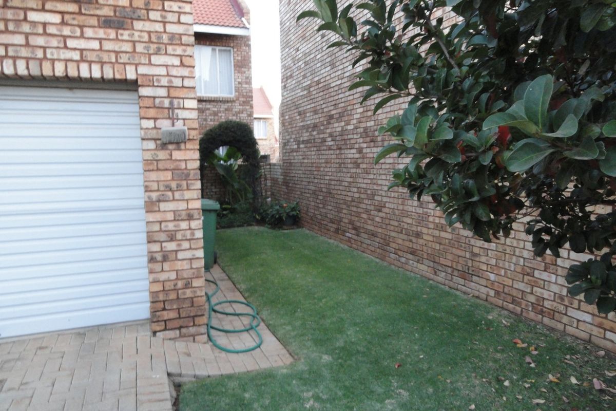 A side view of the townhouse featuring a face brick facade, a roll-up garage door, paved driveway, and a small lawn area.