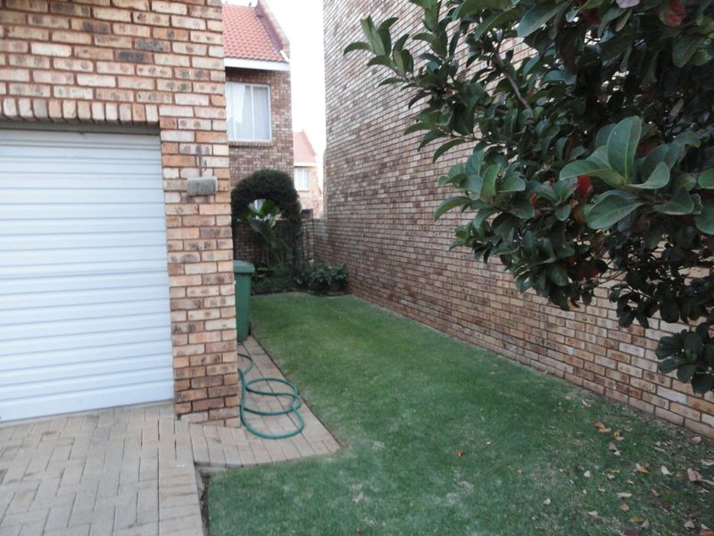 A side view of the townhouse featuring a face brick facade, a roll-up garage door, paved driveway, and a small lawn area.