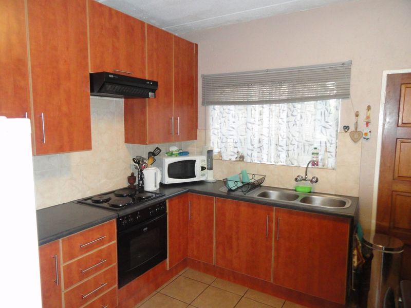 A functional kitchen featuring wood-look cabinetry, dark laminate countertops, a built-in oven with hob, and a double stainless steel sink with tiled backsplash.